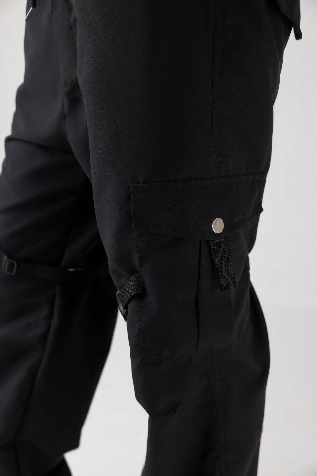 Close-up of thigh straps, micro fabric texture, and waistband detail on black utility cargo pants