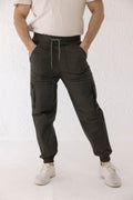 Front view of Thyron cargo pants in olive green twill with black thigh buttons and elasticated hems – Decuir